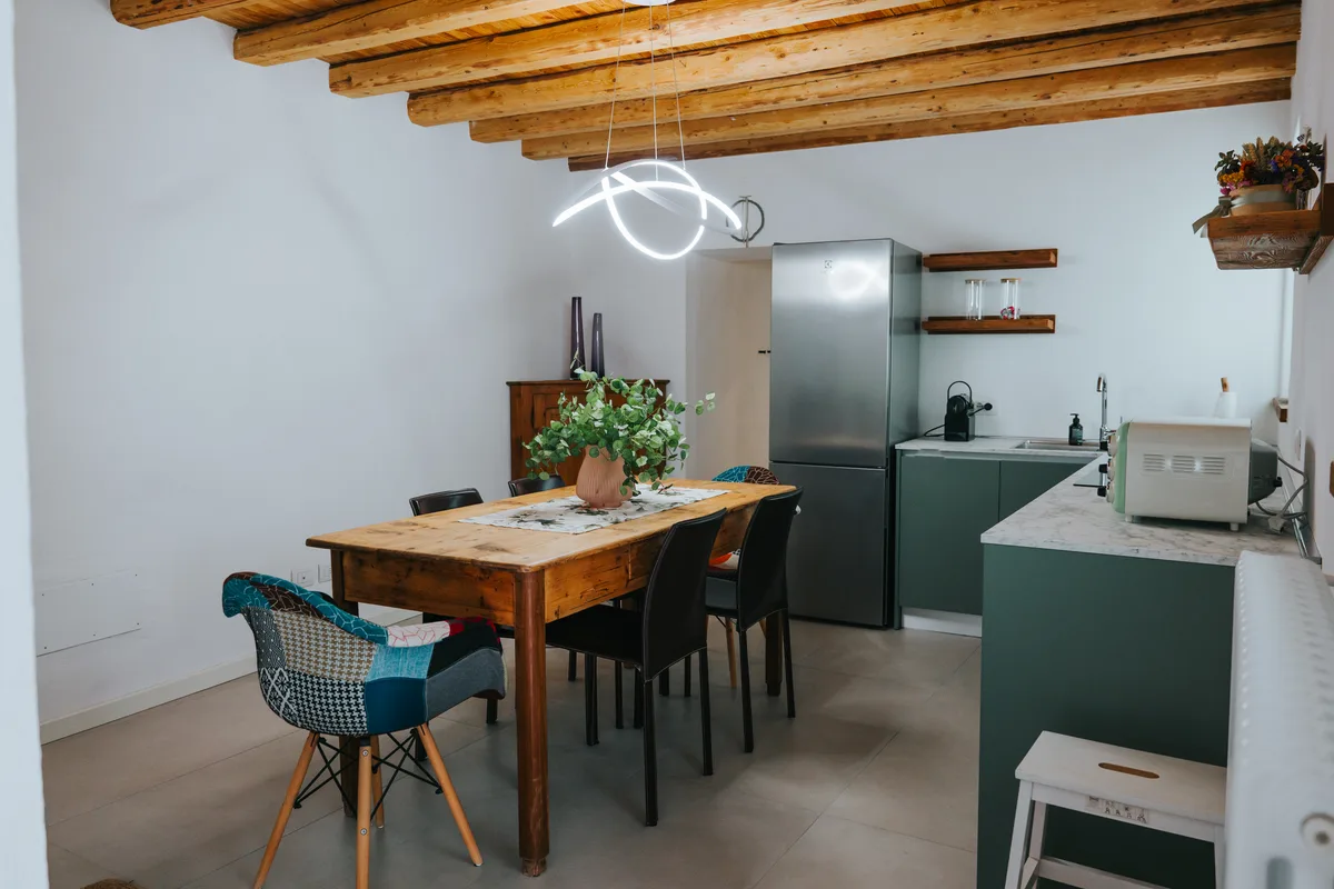 A wooden dining table and sage green kitchen beneath exposed beams